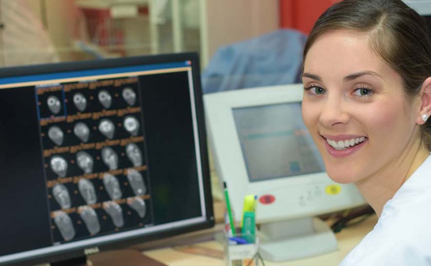 A woman looking at a computer screen displaying multiple brain scan images in a medical setting.