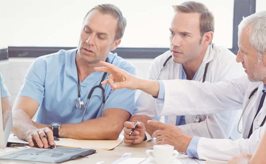 Group of male medical professionals sitting around a table discussing something on a digital device.