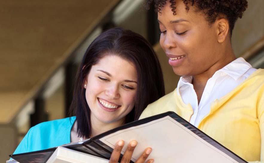 Two women holding and looking at open binders, both are smiling.
