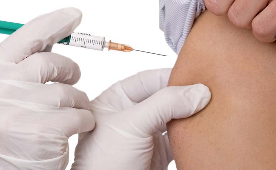 Close up of a healthcare professional wearing white gloves giving an injection to another person on the upper arm.