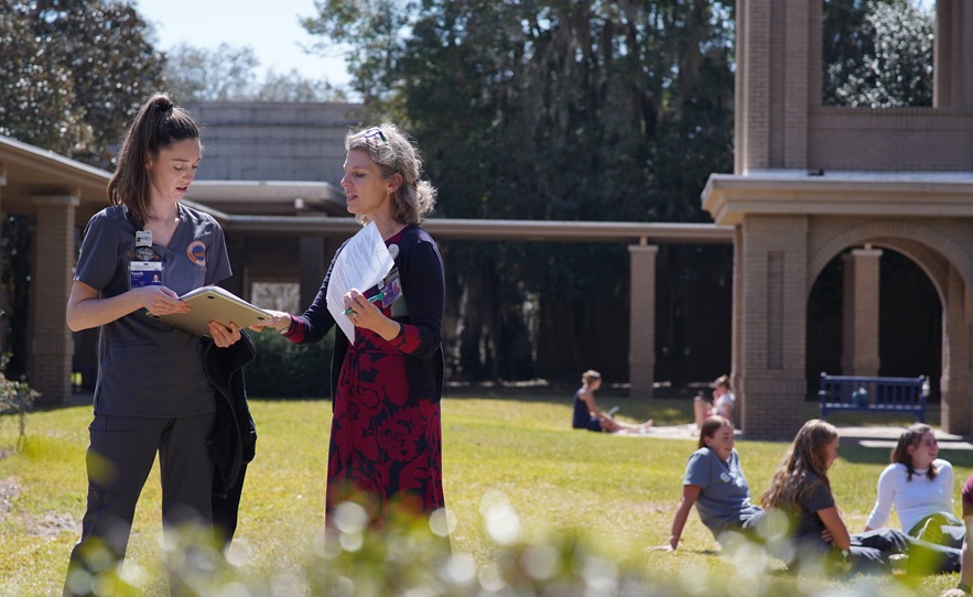 female student wearing South University scrubs speaking to faculty outside the Savannah campus building in the grassy area