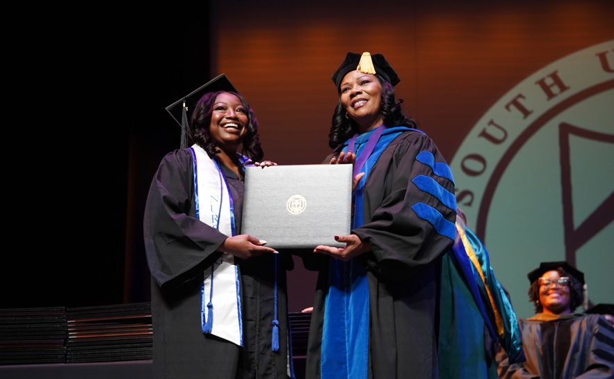 graduation ceremony with a student receiving her diploma by a decorated instructor wearing graduation ceremony gowns