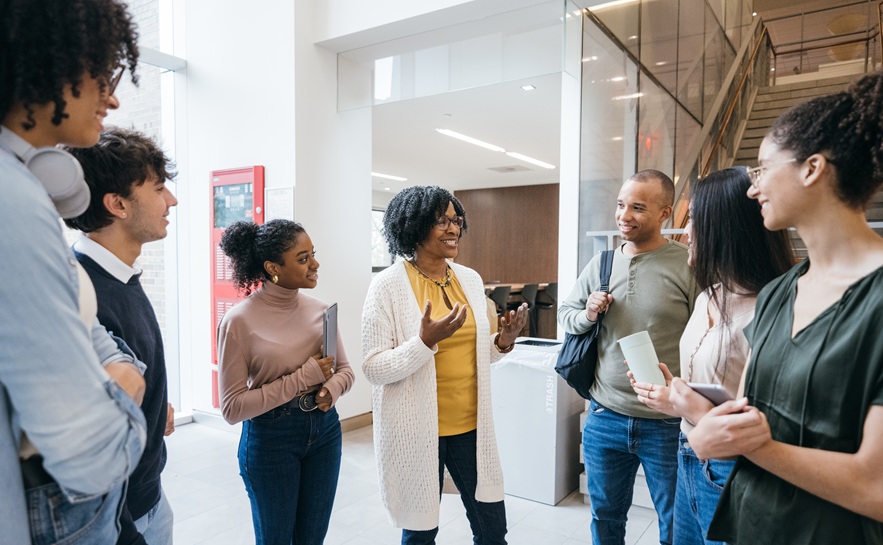 group of six student speaking with an instructor in the hallway